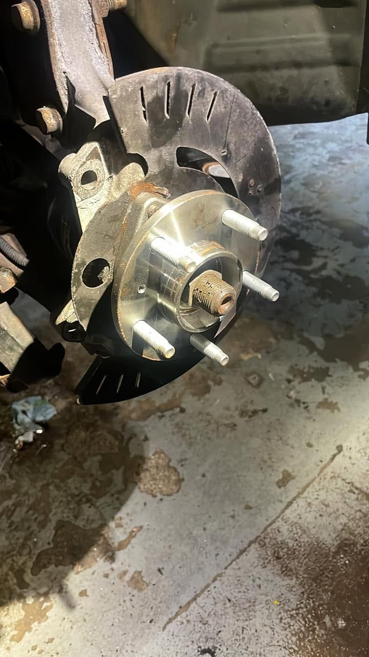 Close-up of a vehicle wheel hub and brake rotor coated with dirt in a garage. | Auto Logic Complete Auto Repairs