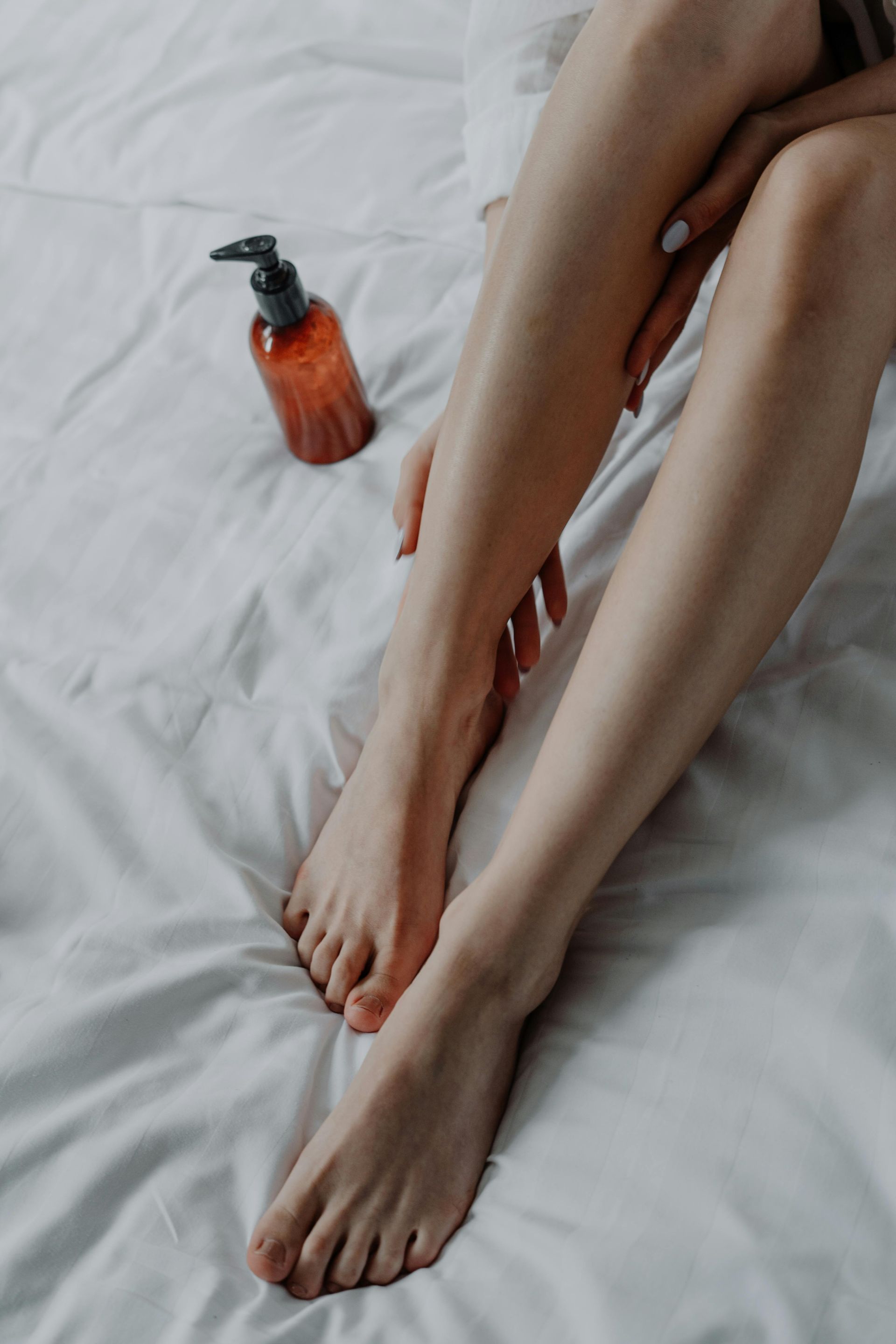 Une femme est assise sur un lit et applique de la lotion sur ses jambes.