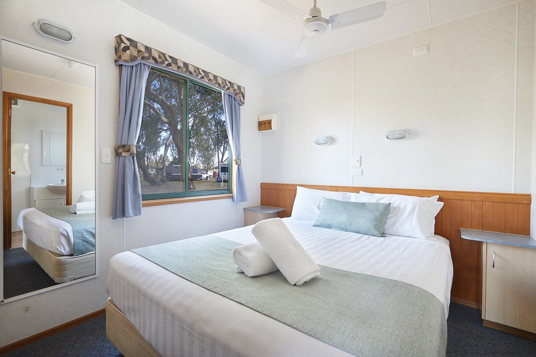 Apex Riverbeach Holiday Park cabin's bed and a window , fan and mirror.