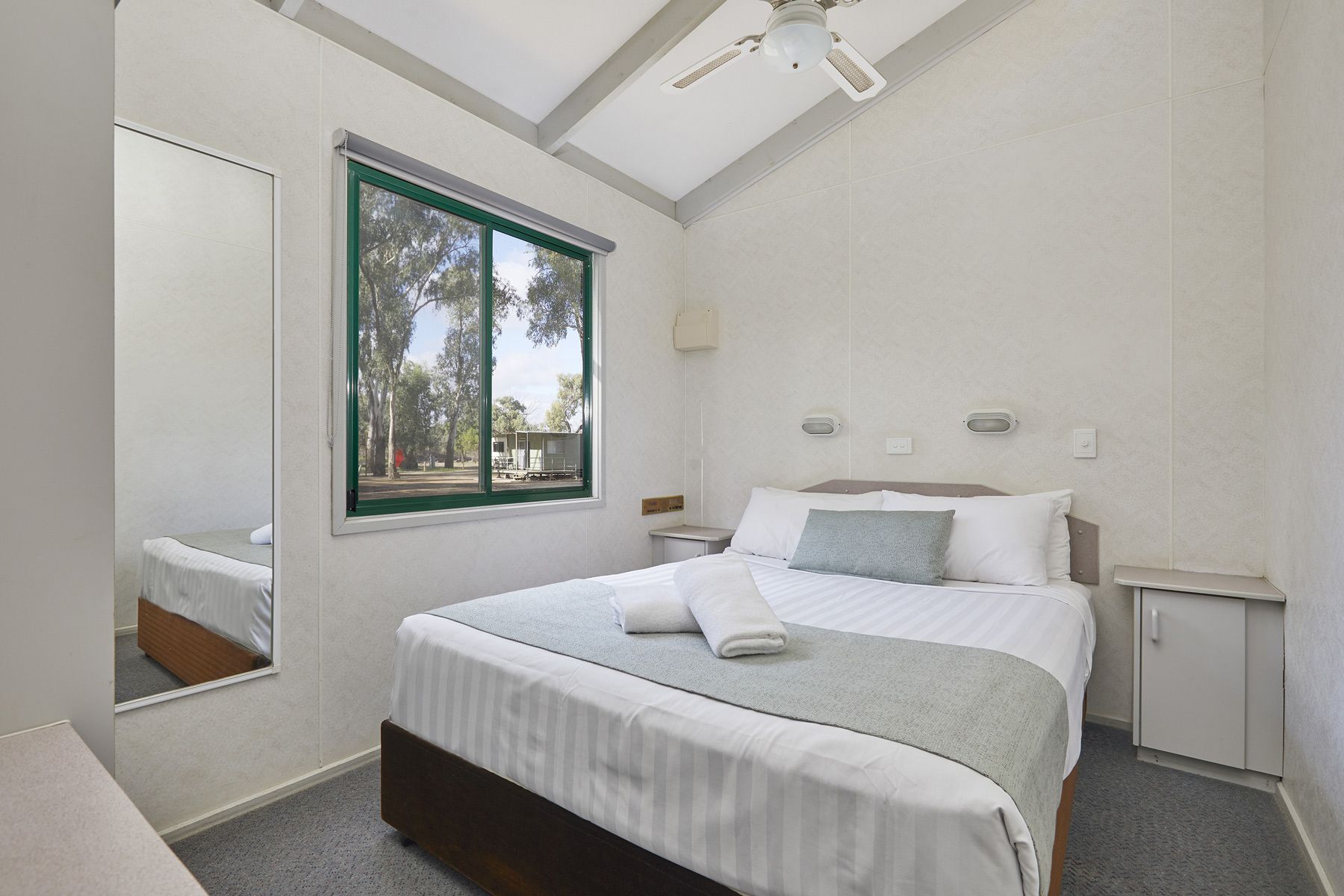Apex Riverbeach Holiday Park cabin's bedroom with a bed , a mirror and a window .