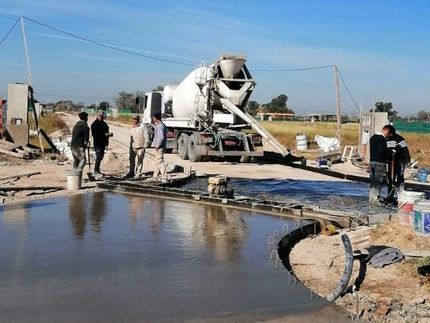 En un día soleado, unos obreros de la construcción supervisan un camión hormigonera que vierte hormigón para construir una nueva superficie de carretera.