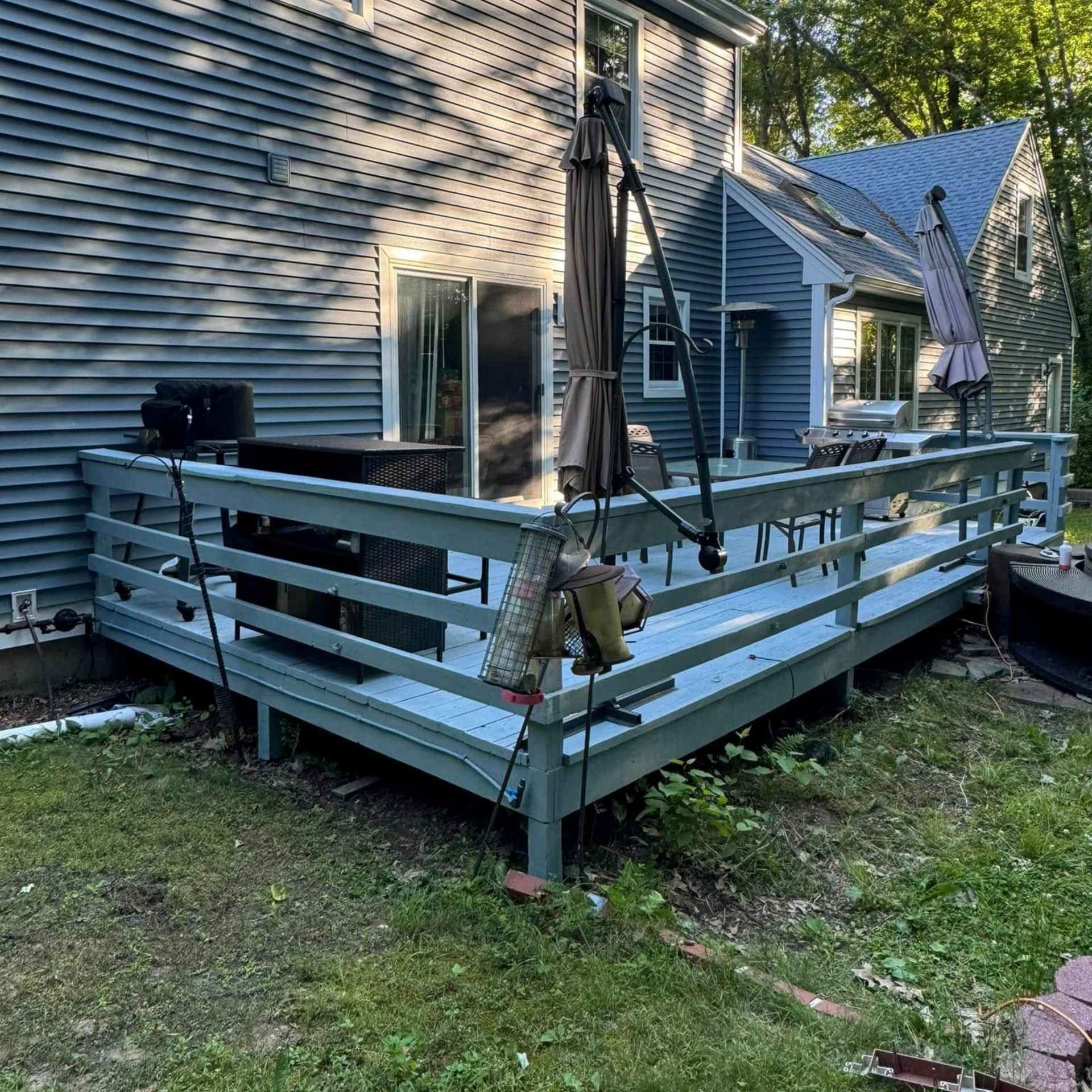 Raised backyard deck with light blue railings, closed patio umbrella, and house siding beside a grassy yard