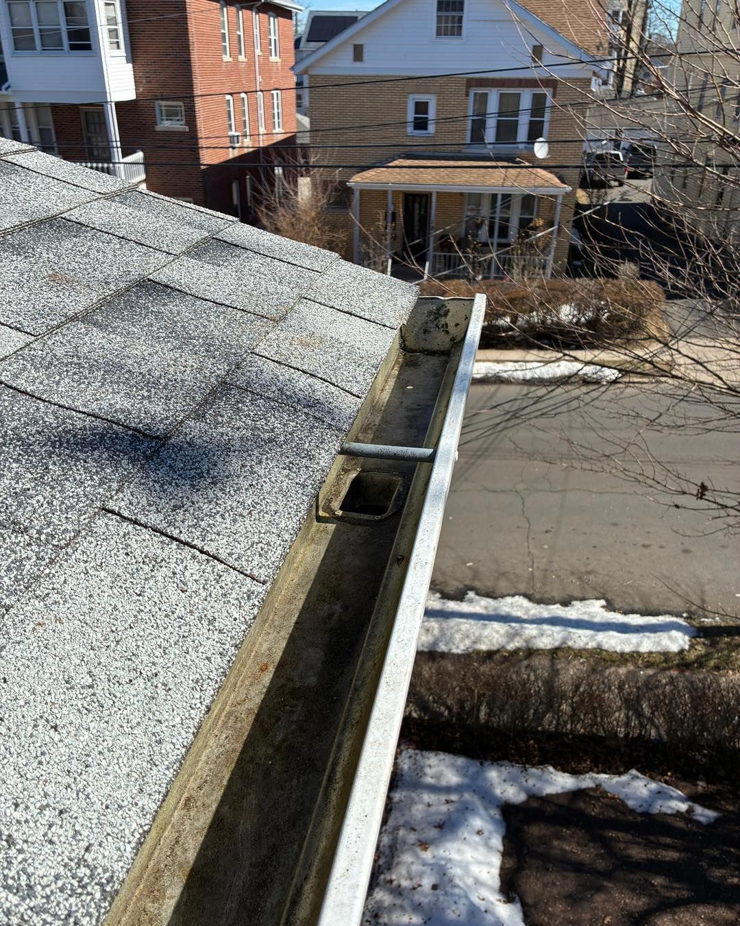 Rooftop gutter above a residential street with houses and patches of snow below