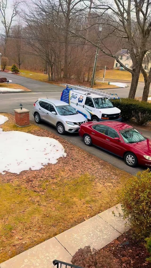 Snowy driveway with three parked cars beside a suburban street and leafless trees