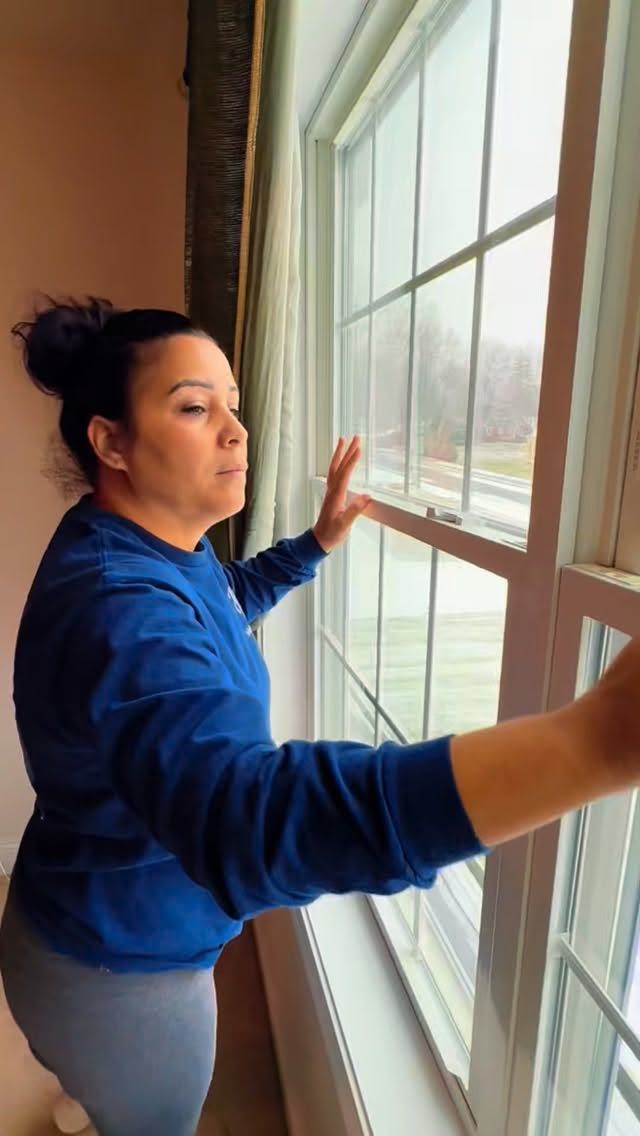 Person in a blue hoodie opening a window and looking outside.
