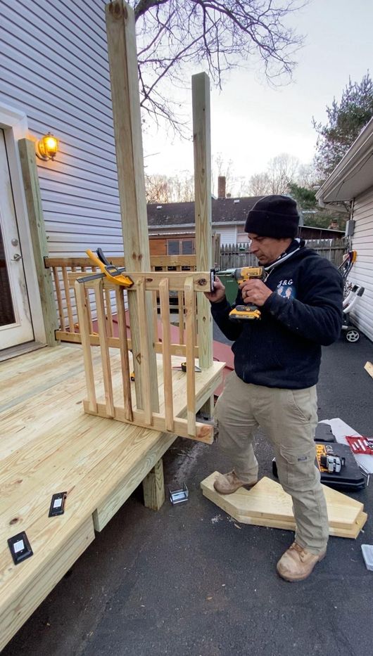 Person assembling a wooden porch railing beside a house, with tools and lumber on the steps
