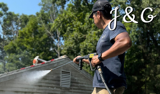 Worker using a nail gun on a roof under a blue sky, with “J&G” text in the corner