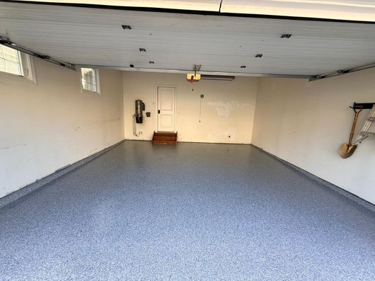 Empty garage interior with gray speckled floor, white walls, and closed door at the far end