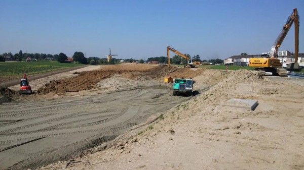 Bouwplaats met zware machines, waaronder drie graafmachines, die grond verplaatsen op een zonnig, open veld.
