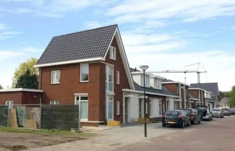 Een straatbeeld van moderne, in aanbouw zijnde rijtjeshuizen van rode baksteen, met auto's ernaast geparkeerd.