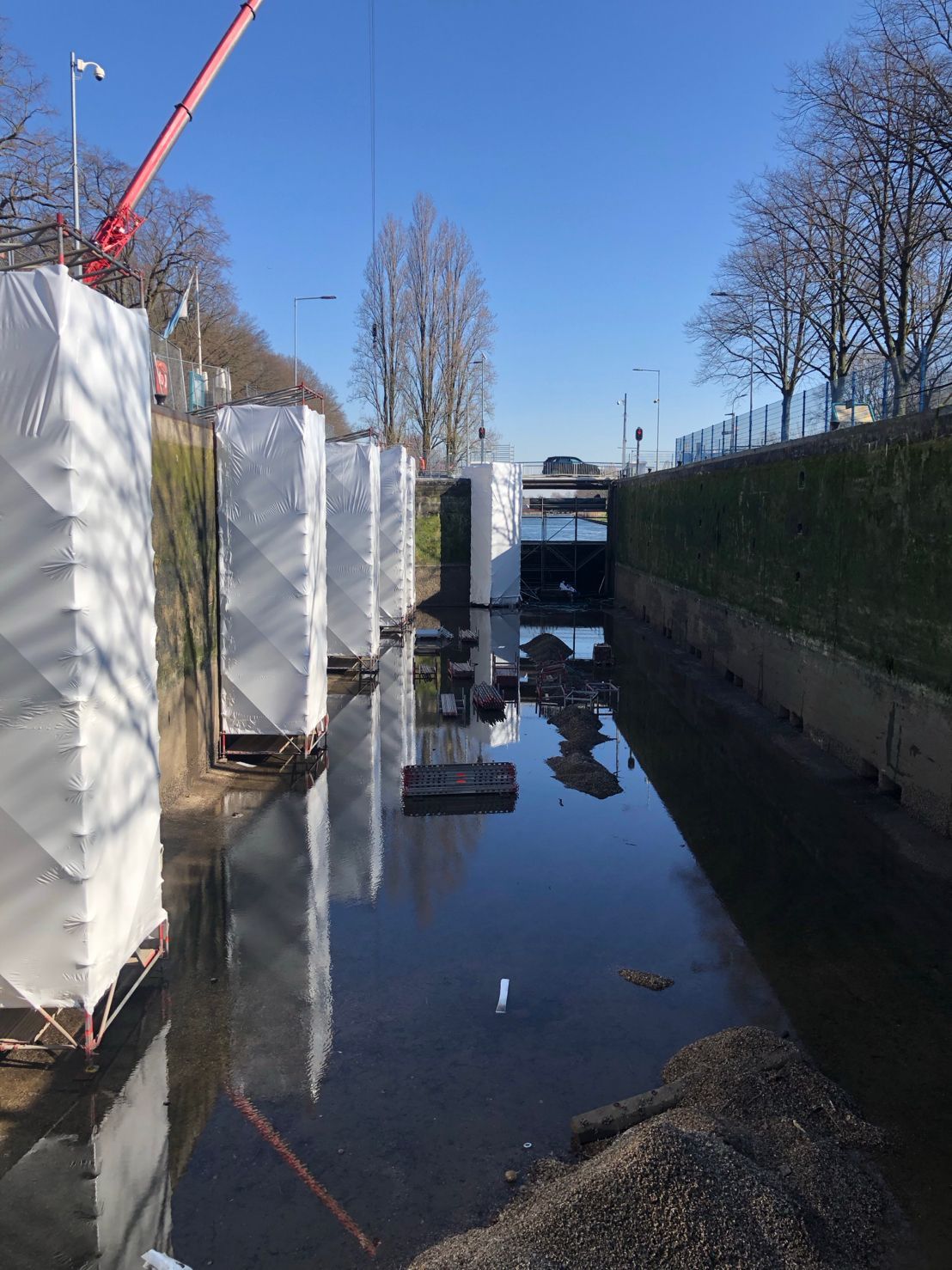 Hoge, wit omwikkelde pilaren staan ​​in een smal kanaal onder een helderblauwe hemel, met een kraan erboven zichtbaar.