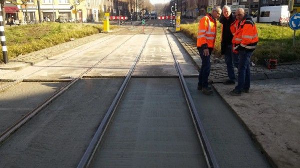 Drie personen in oranje, reflecterende hesjes staan ​​bij een pas aangelegde tramrails tijdens wegwerkzaamheden overdag.