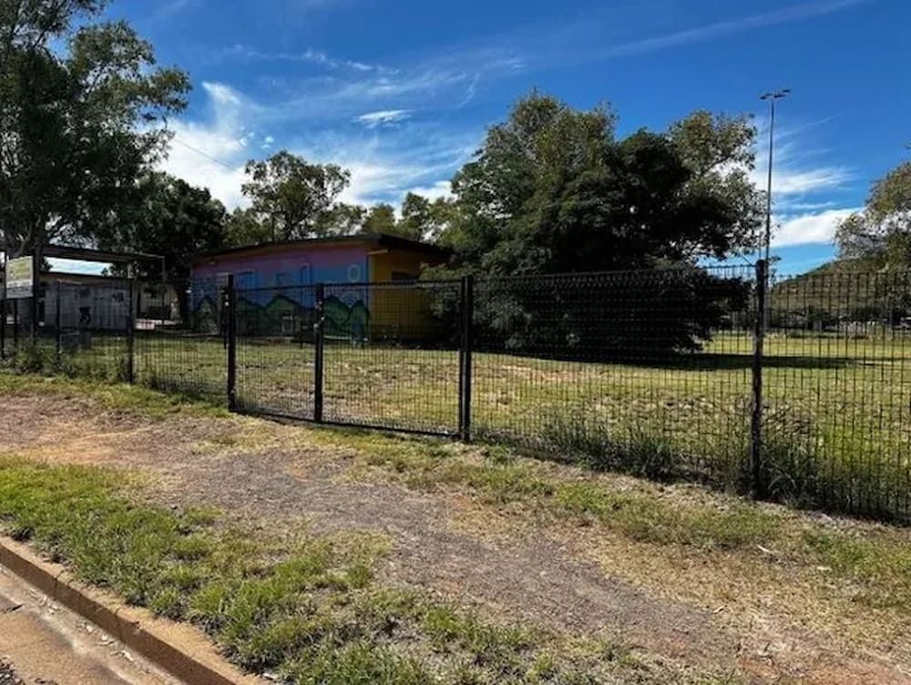 A Fence Surrounds A Grassy Field With A Building In The Background — PH Davie in Boulia, QLD