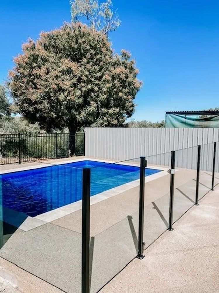 A Large Swimming Pool Surrounded By A Glass Fence With A Tree — PH Davie in Cloncurry, QLD
