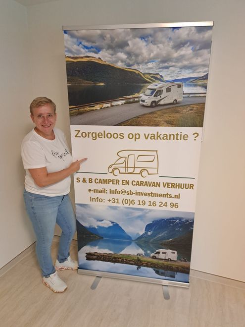Person posing beside a travel banner with a campervan and coastal scenery, reading “Zorgeloos op vakantie?”