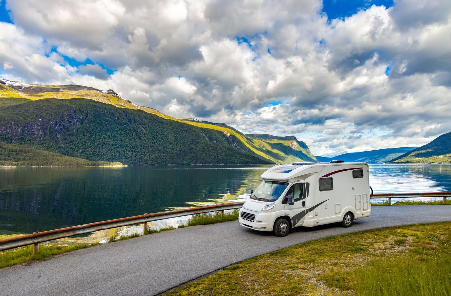 Witte camper geparkeerd aan een fjord met bergen en een bewolkte hemel op de achtergrond.