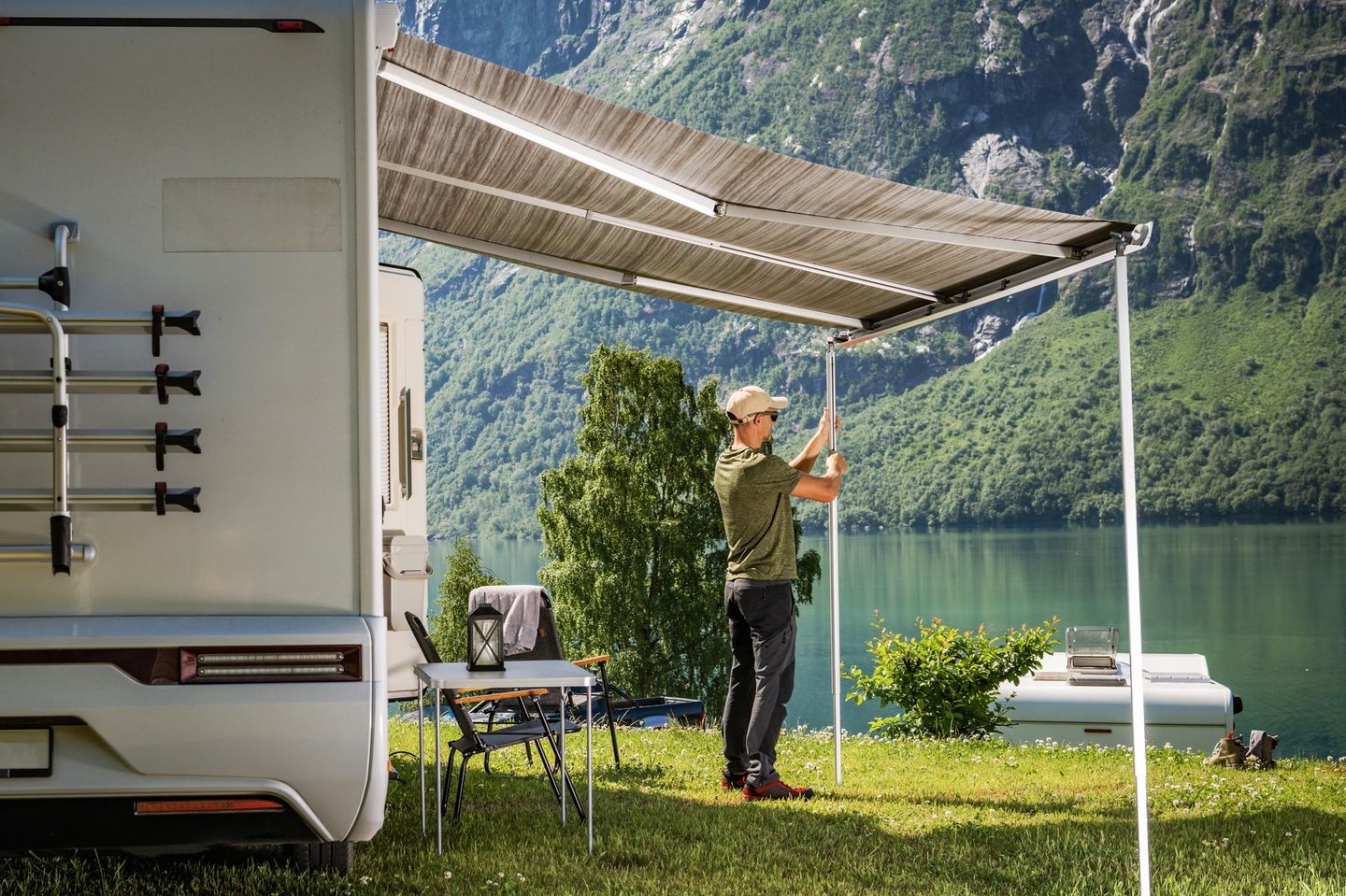 Een persoon vist naast een camper onder een afdak aan een rustig bergmeer.