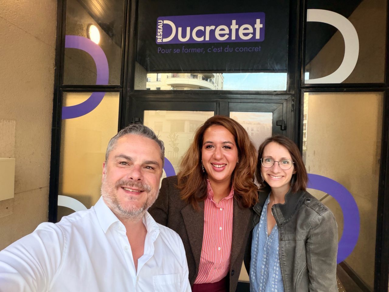 Three people smiling outside Ducretet storefront, with purple window accents behind them.