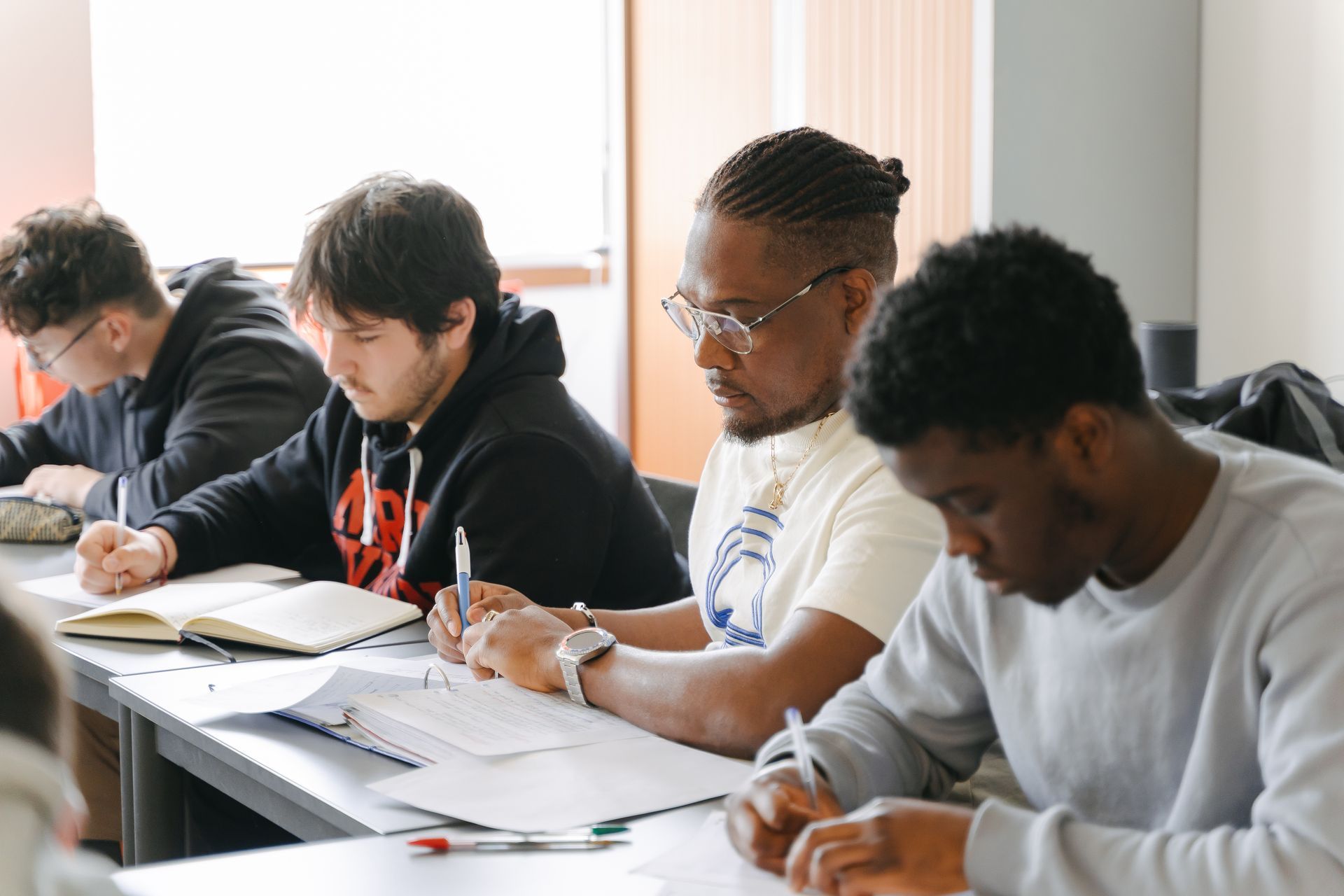 Un groupe de jeunes hommes sont assis à des tables dans une salle de classe.