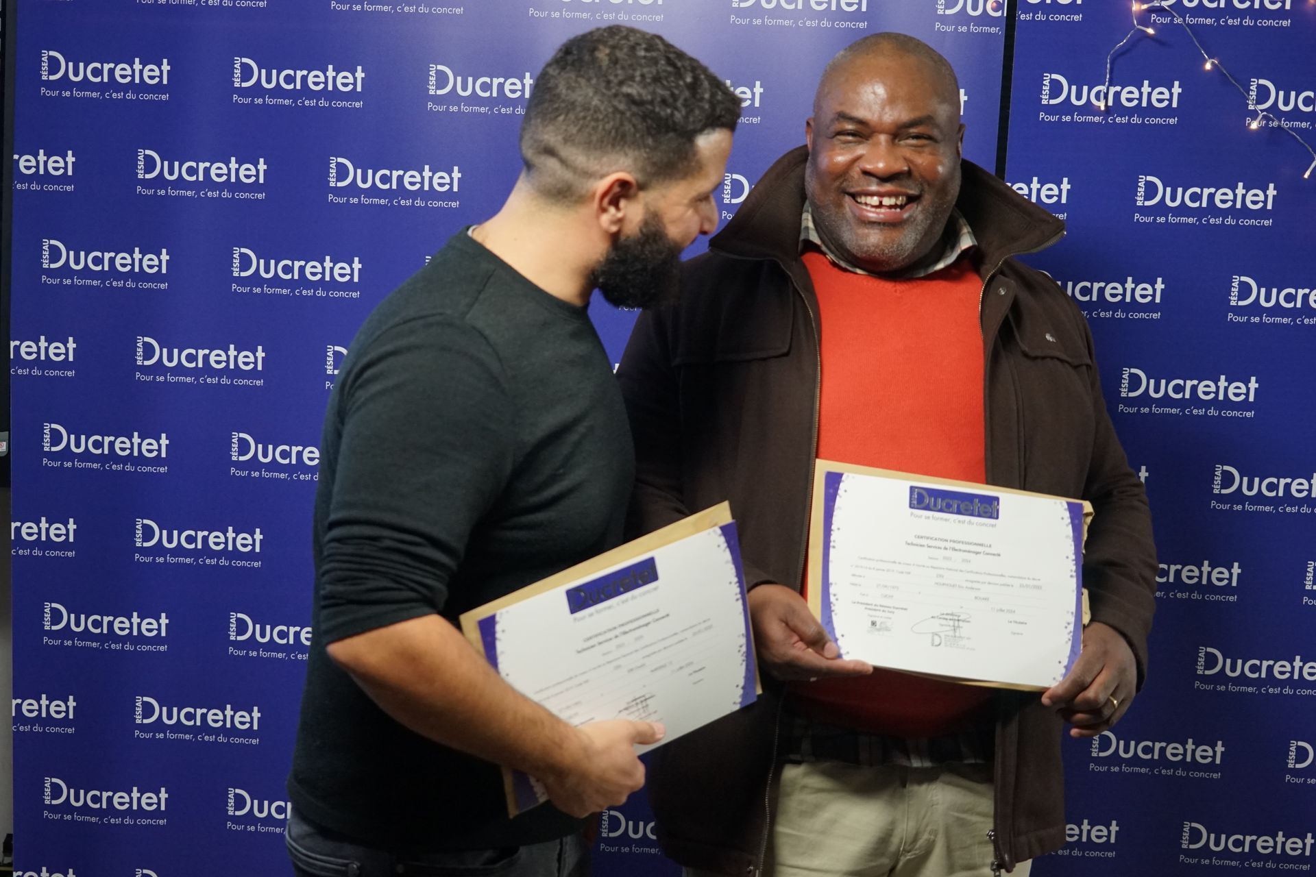 Deux hommes tiennent des certificats devant un mur sur lequel est écrit ducretet
