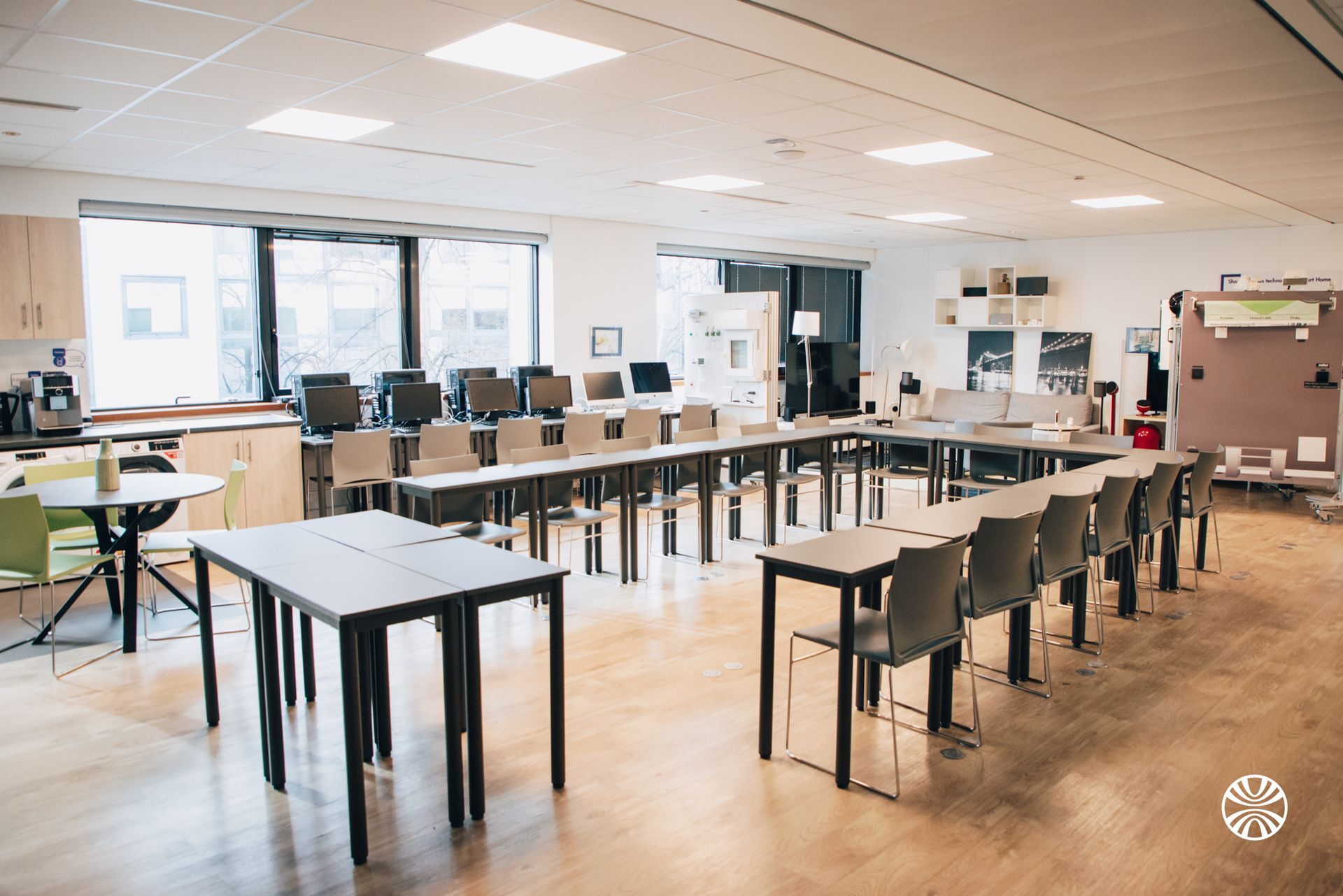 Salle de classe avec des tables disposées en U, des ordinateurs le long du mur du fond et des chaises.