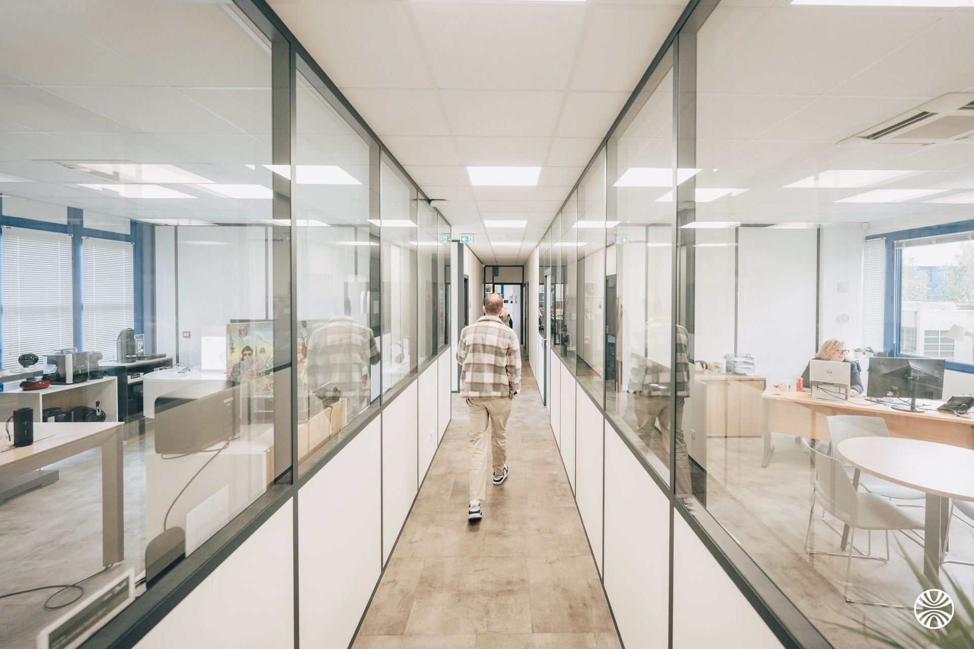 Une personne marchant dans un long couloir de bureau avec des pièces aux parois vitrées.