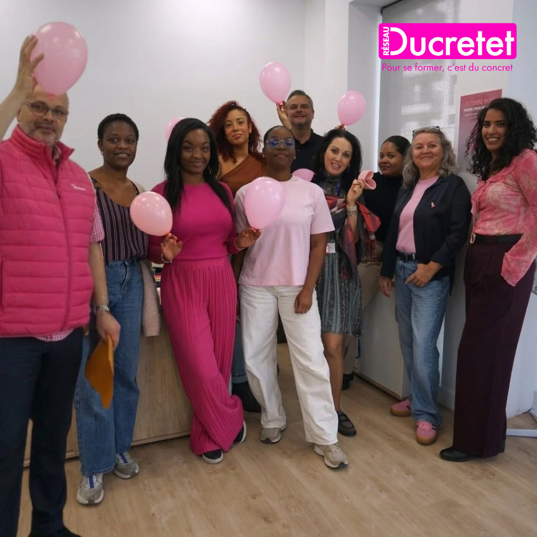 Group posing with pink balloons in a Ducretet office, wearing pink and white outfits.
