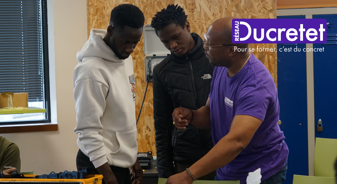 Three people in a workshop gather around equipment, one in a purple shirt gesturing near a window.