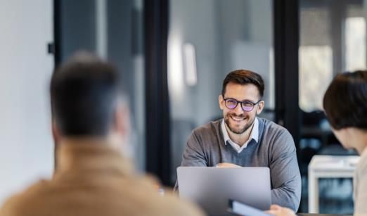 Un homme portant des lunettes sourit en regardant deux personnes assises