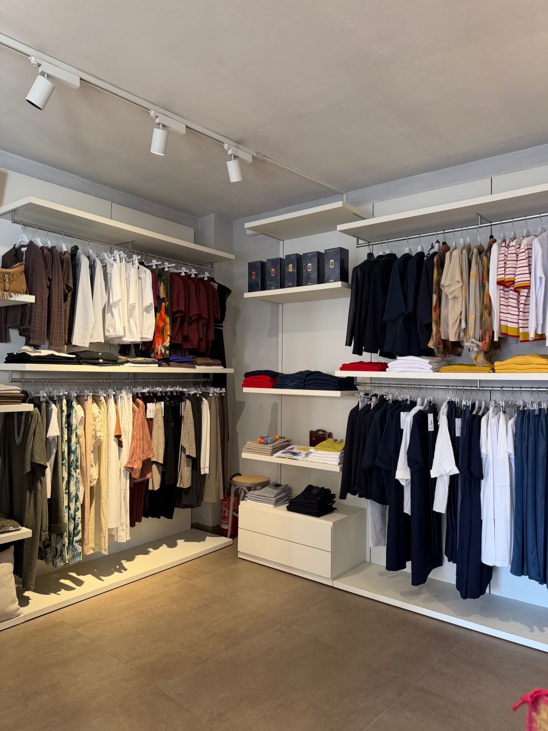 Boutique di abbigliamento con scaffali pieni di camicie e giacche disposte ordinatamente in una stanza luminosa e minimalista.
