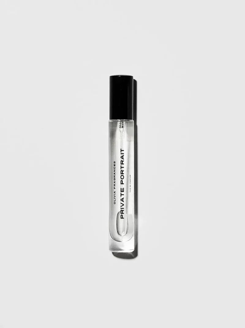 Flacone di profumo trasparente con tappo nero su sfondo grigio chiaro.
