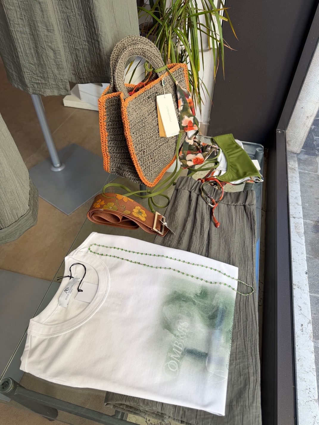 Pantaloncini bianchi con occhiali da sole e una macchia verdastra sotto un piccolo albero esposto in una vetrina.