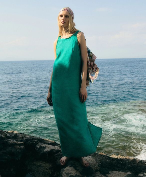Una persona con un vestito color verde acqua è in piedi su degli scogli in riva al mare, con l'oceano alle spalle.