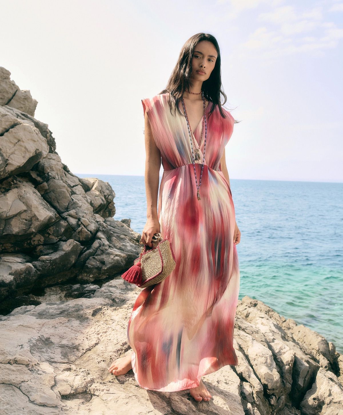 Donna in abito rosa in piedi su una costa rocciosa in riva al mare