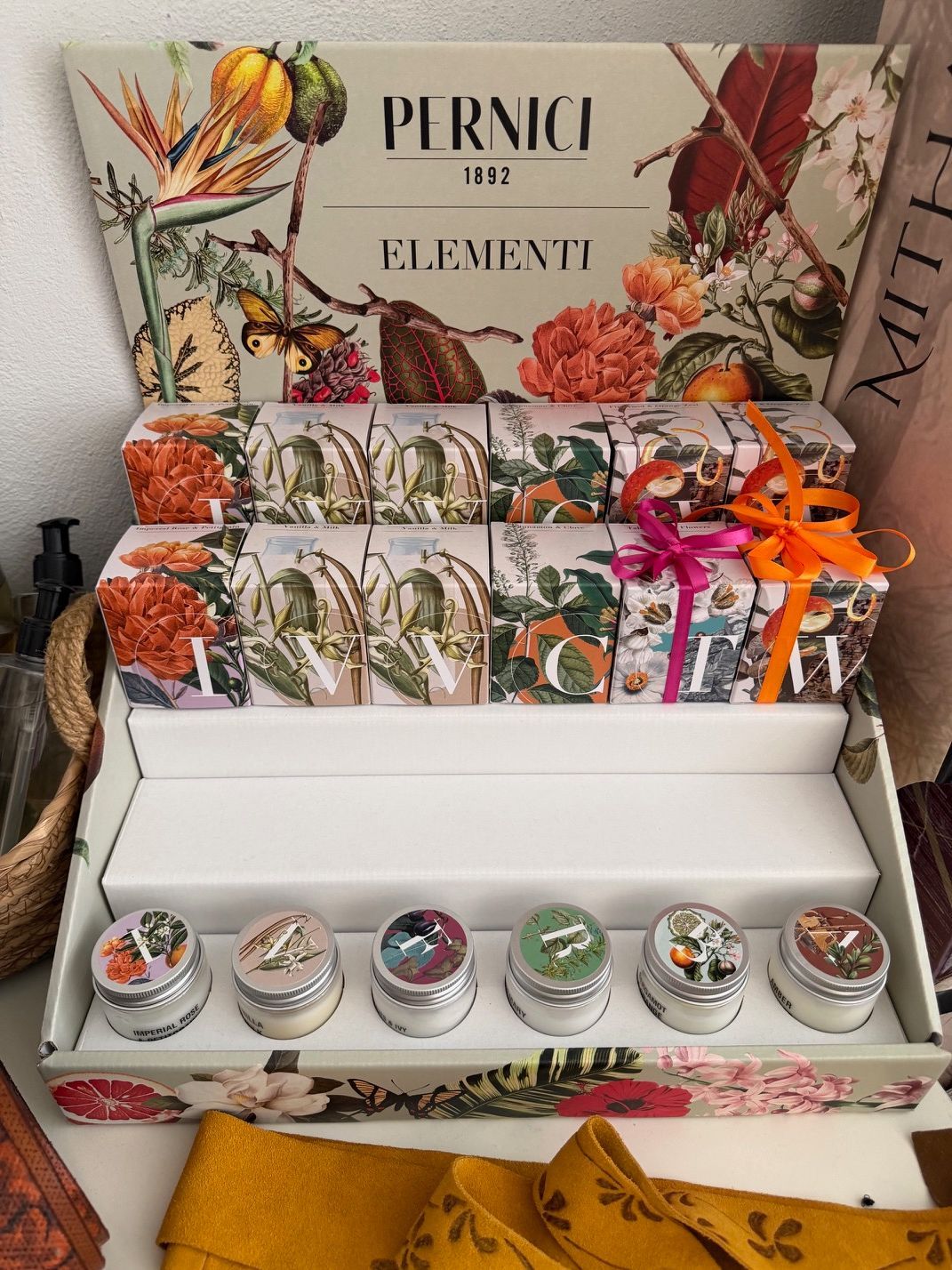 Espositore regalo decorato con piccoli vasetti, oggetti incartati, fiori arancioni e un fiocco dorato con le scritte 