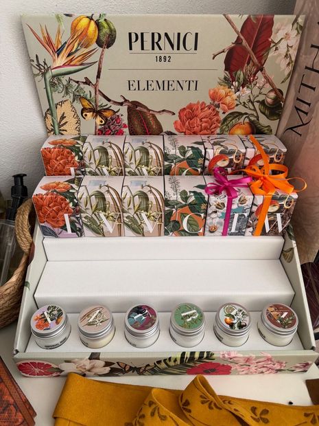 Espositore regalo decorato con piccoli vasetti, oggetti incartati, fiori arancioni e un fiocco dorato con le scritte