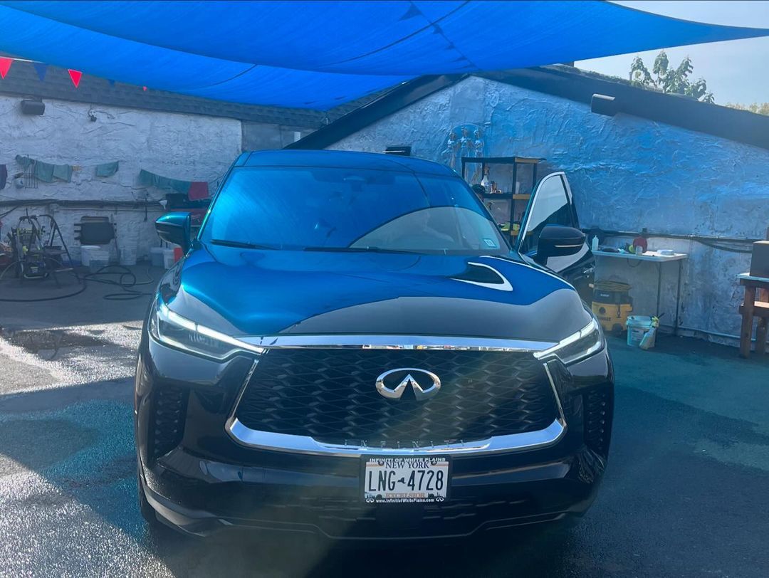 A black infiniti q50 is parked under a blue umbrella.