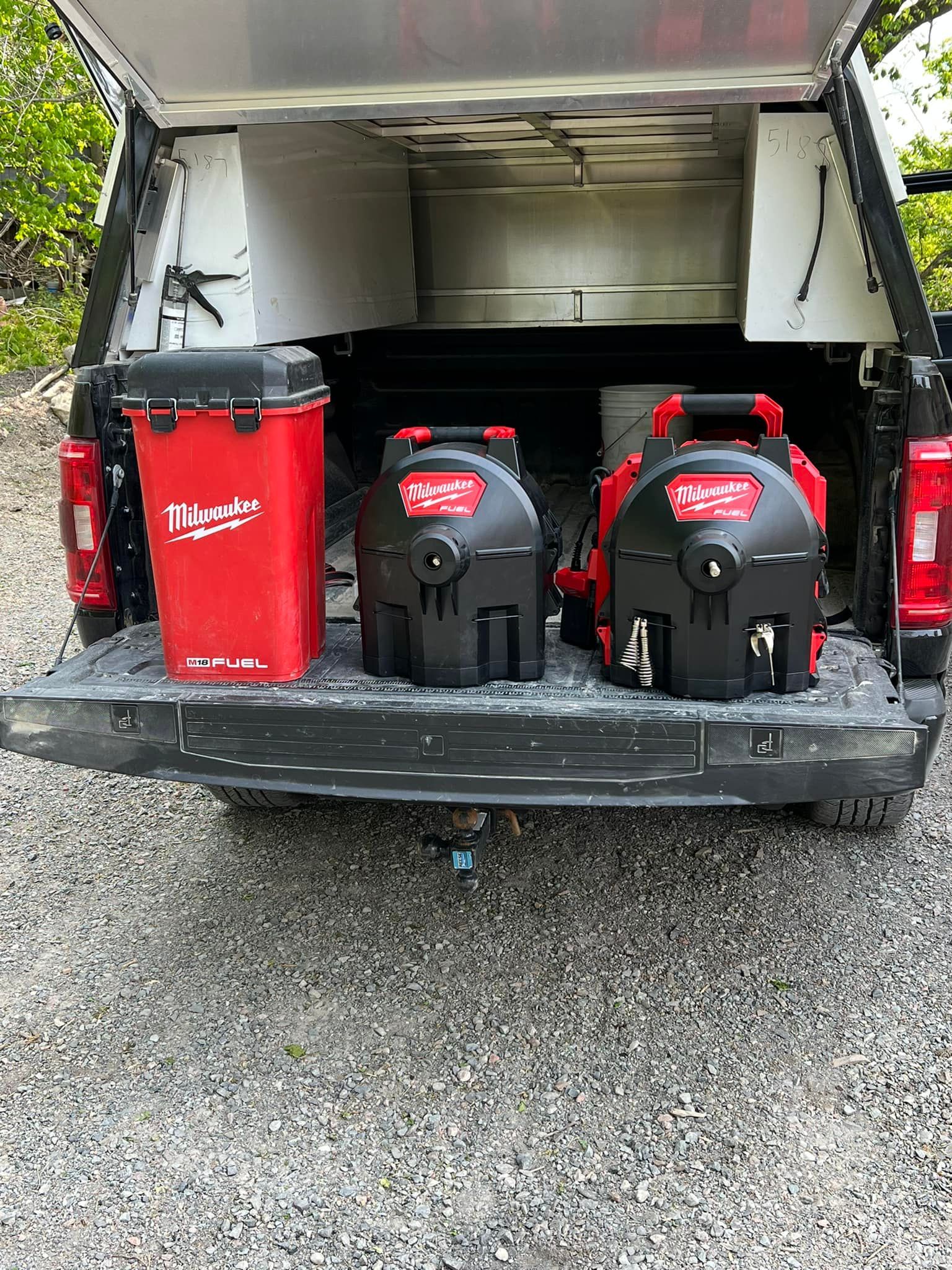 A truck bed with a red cooler and two red and black power washers under a canopy. The tailgate is down on a textured surface.