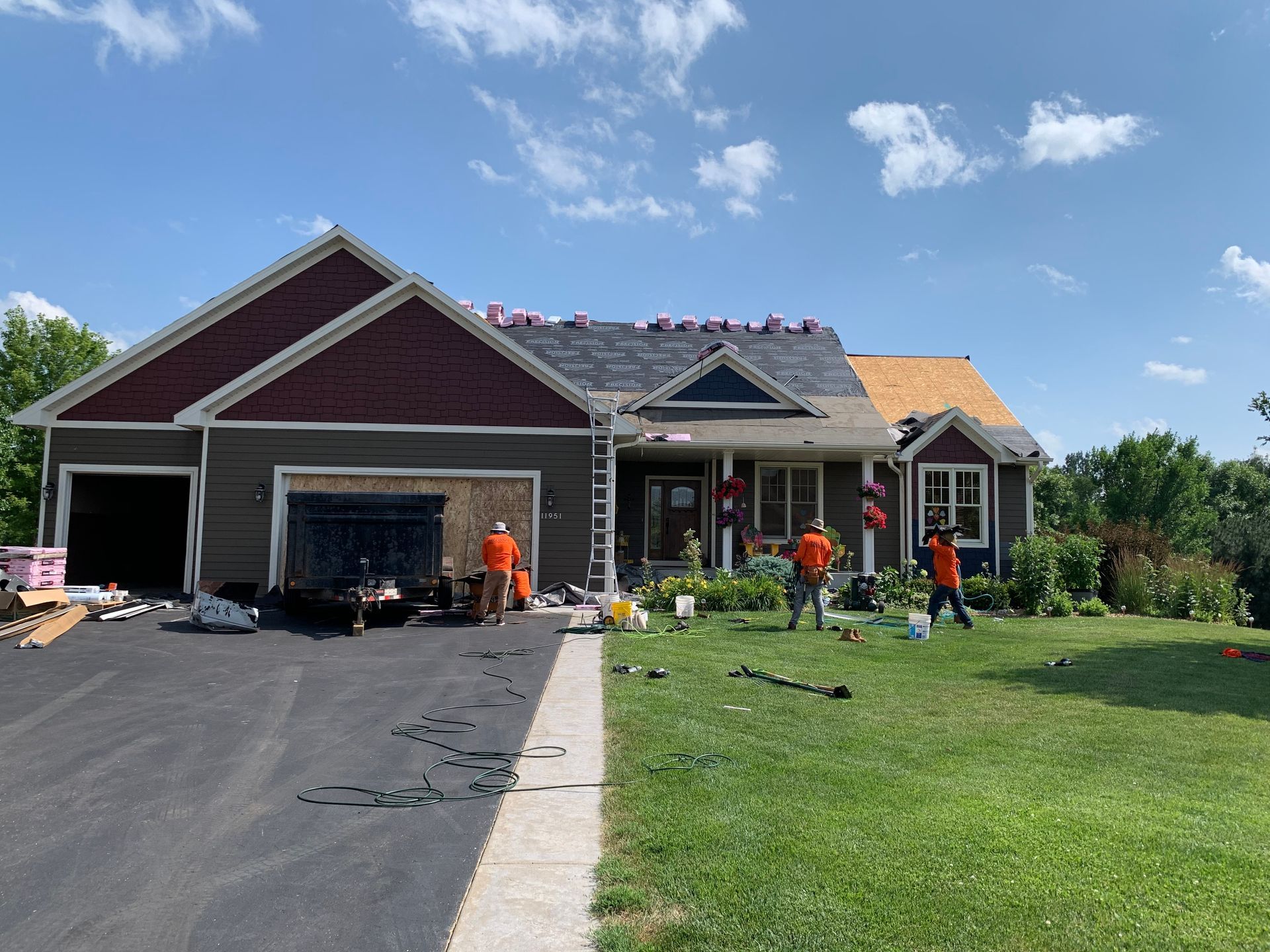 Roofing crew working on home renovation, installing shingles on a residential property with landscaped yard, showcasing Precision Exteriors Restoration services.