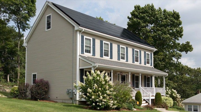 Two-story residential home with solar panels, surrounded by greenery, showcasing siding and windows, relevant to local roofing and exterior services in Denver.