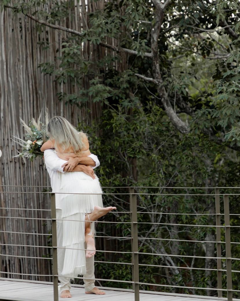 Person in white clothing holding a large bird near a fenced, leafy outdoor area.