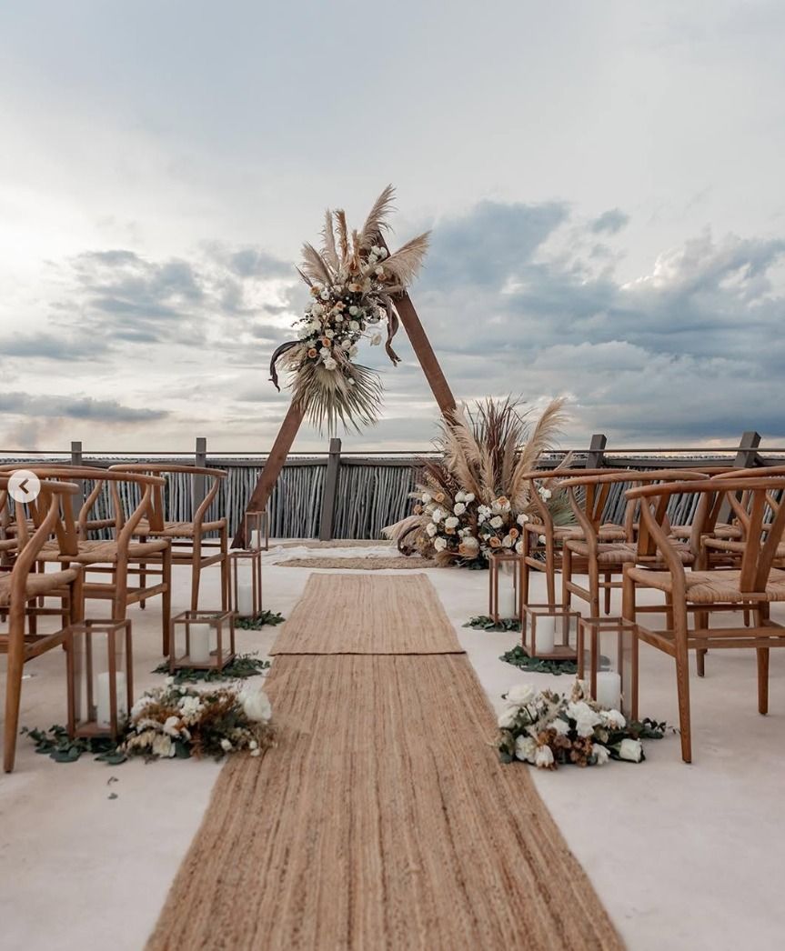 Beach wedding aisle with wooden arch, floral arrangements, and rows of chairs at sunset