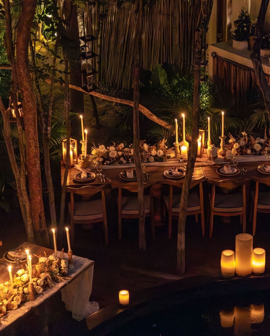 Candlelit tropical dining table with flowers, candles, and hanging greenery by the water