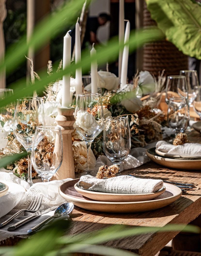 Elegant candlelit dining table with white dishes, glassware, and greenery centerpiece