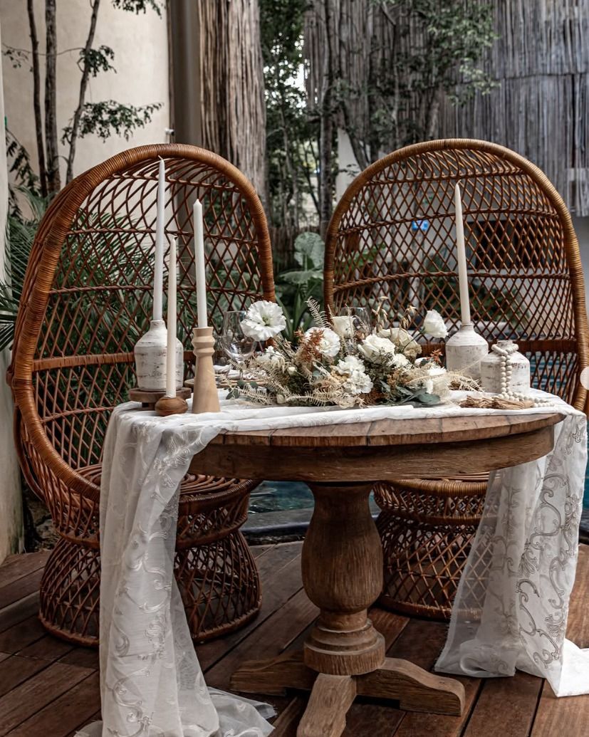 Rustic outdoor table with white lace decor, candles, flowers, and wicker chairs