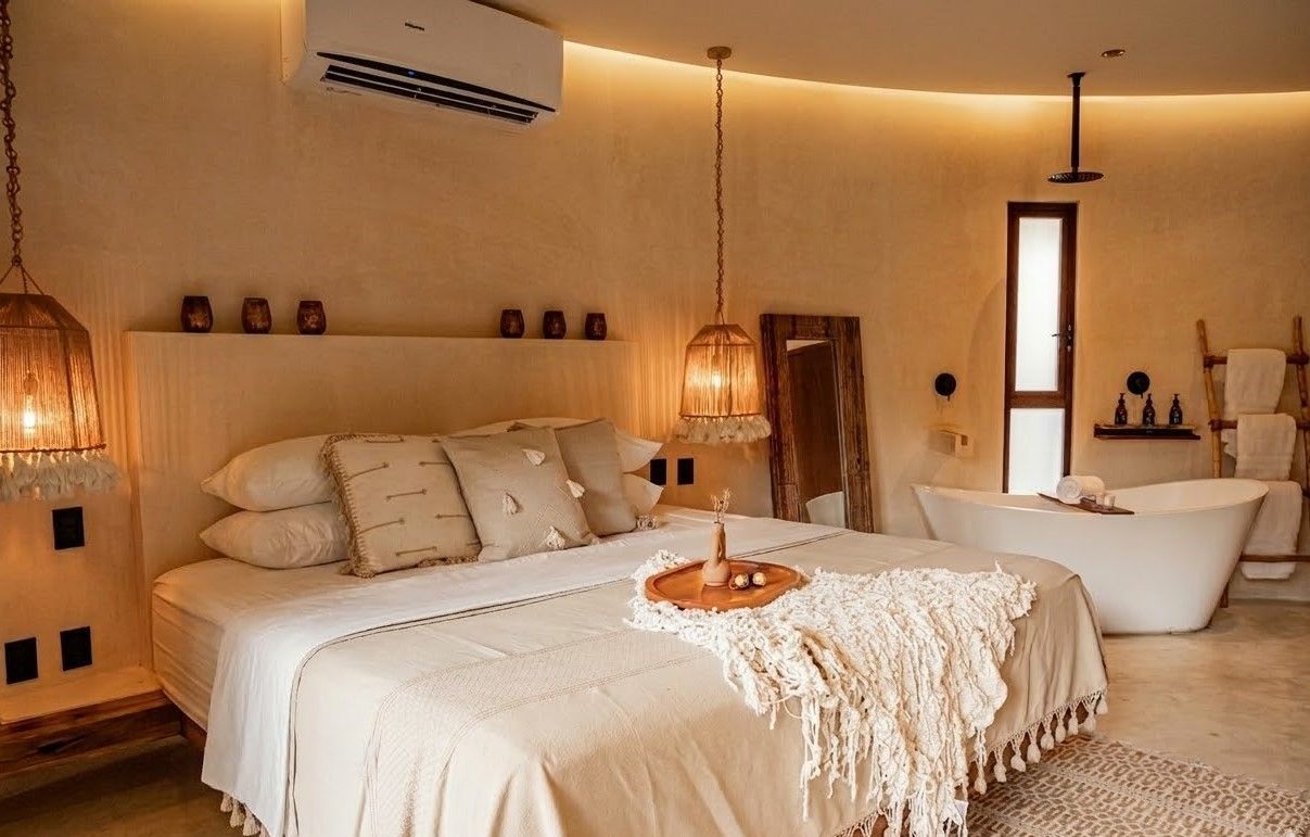 Cozy beige bedroom with a bed, hanging lamps, a freestanding tub, and warm boho decor
