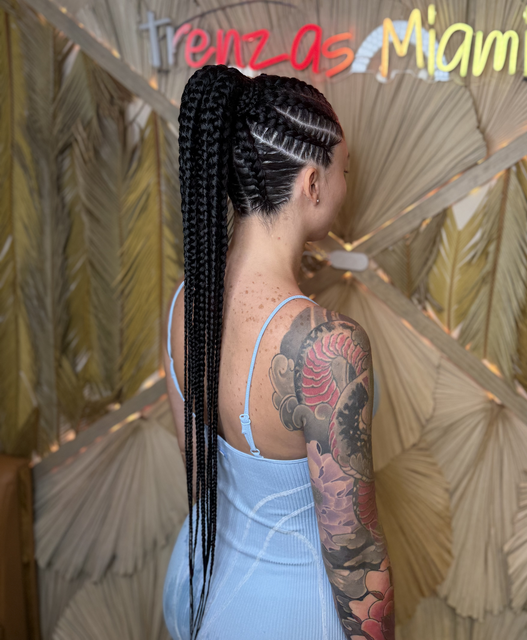A woman with braids and a tattoo on her arm is wearing a blue dress.