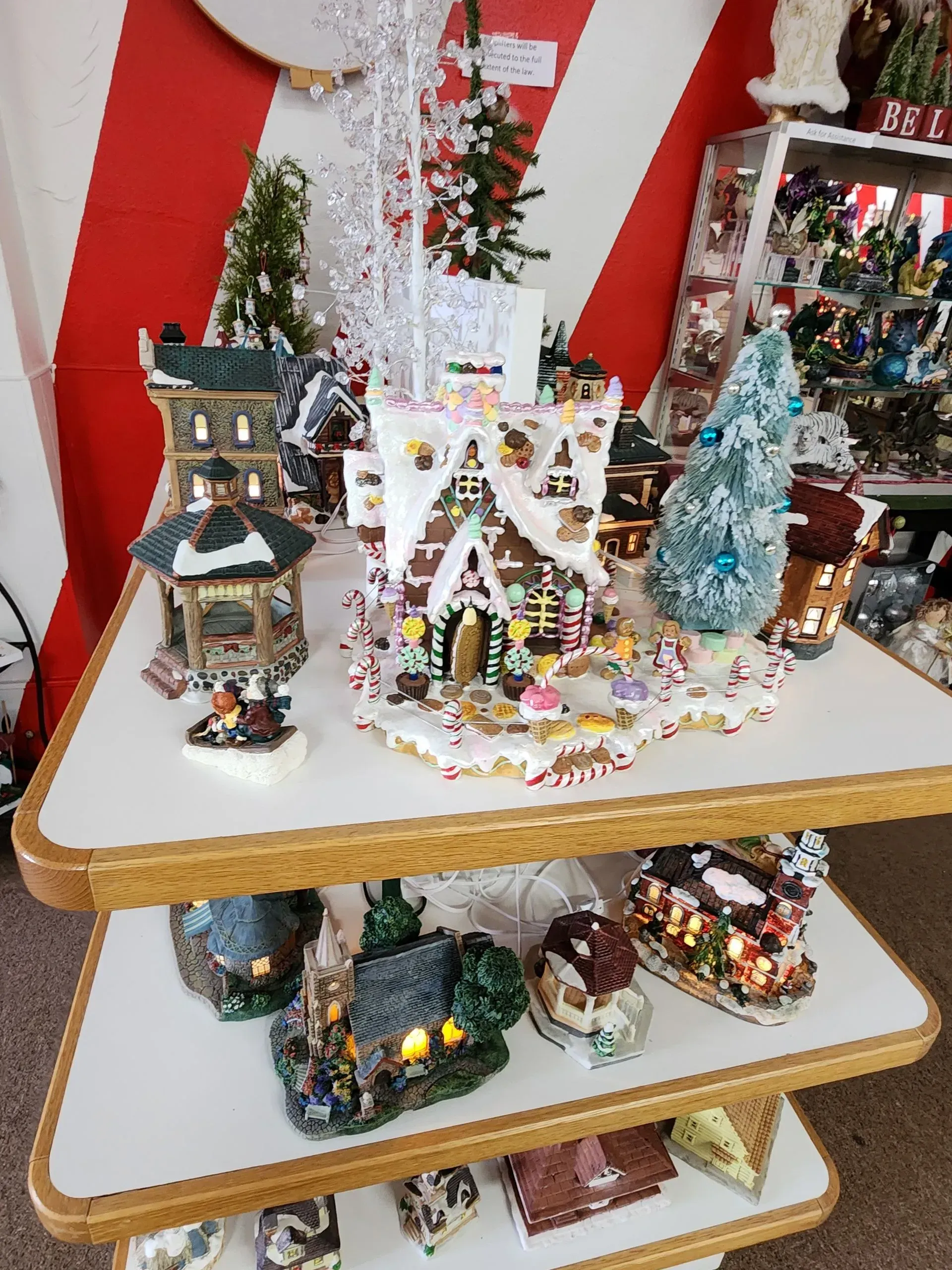Christmas village display on tiered shelves with a gingerbread house as the focal point.