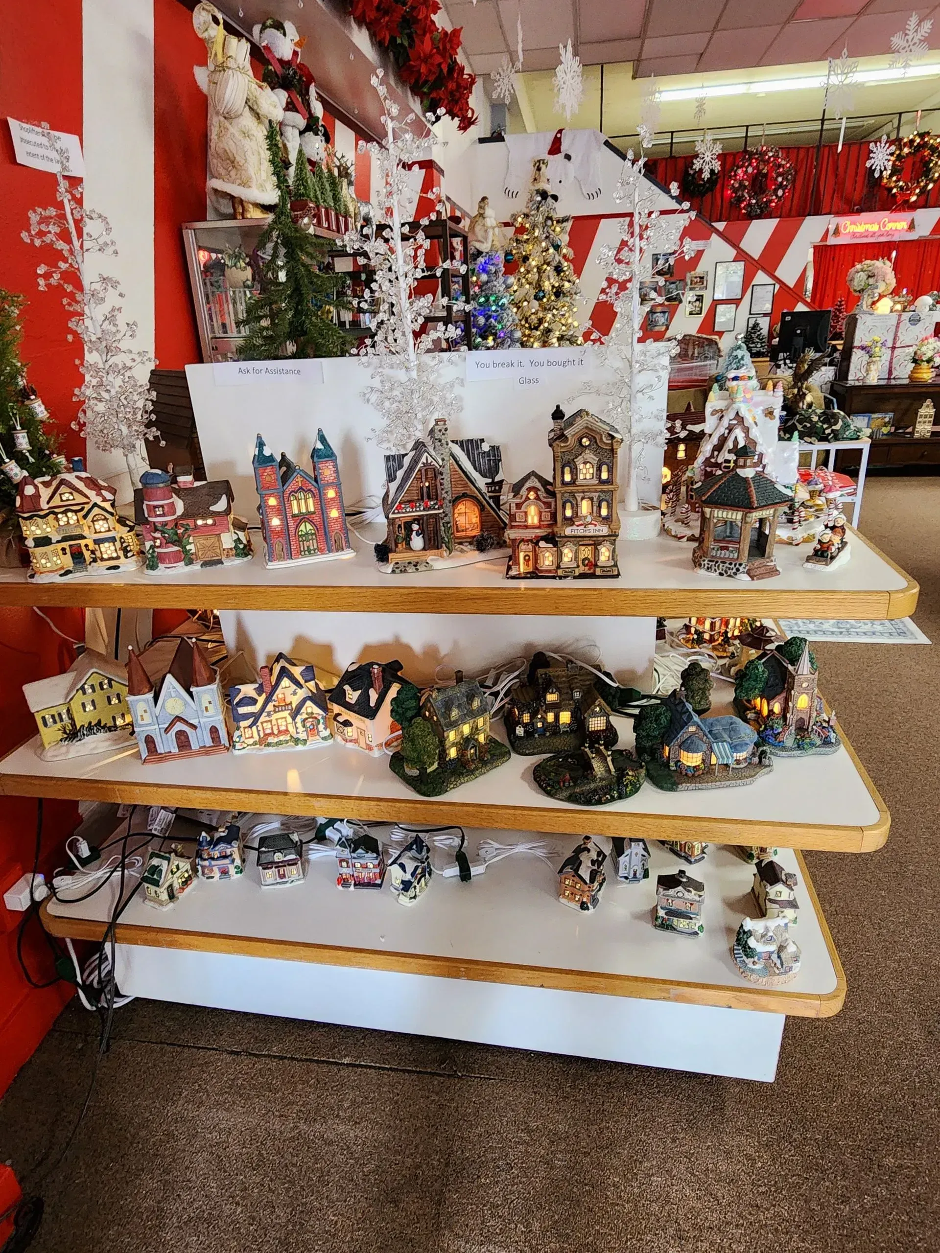 Shelves displaying a Christmas village, decorated with lights and figurines, inside a store.