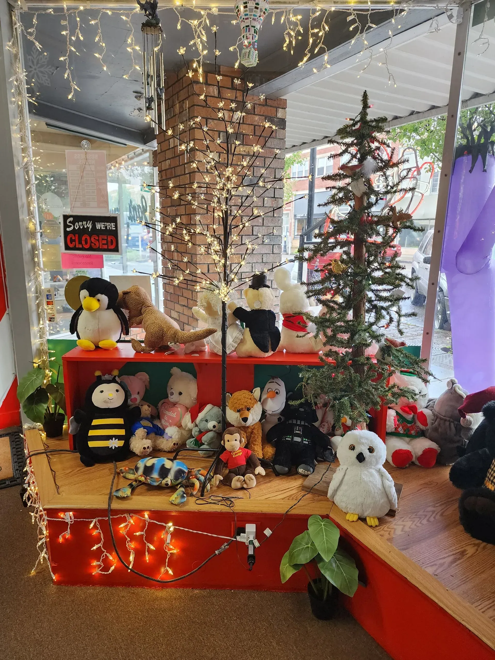 A display with stuffed animals and a small Christmas tree. Red and white display with string lights.